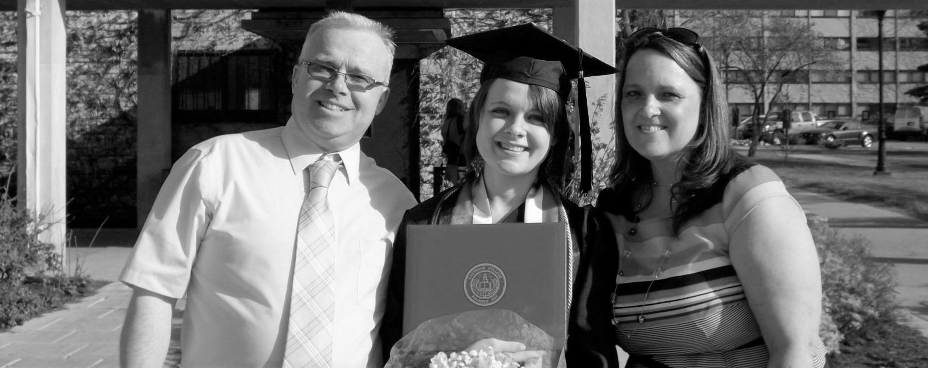 Ashley with her parents either side in full graduation robes holding a diploma and flowers